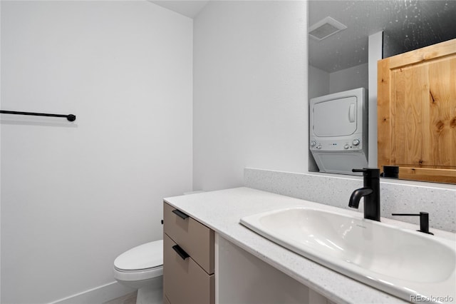 bathroom with vanity, stacked washer and clothes dryer, and toilet