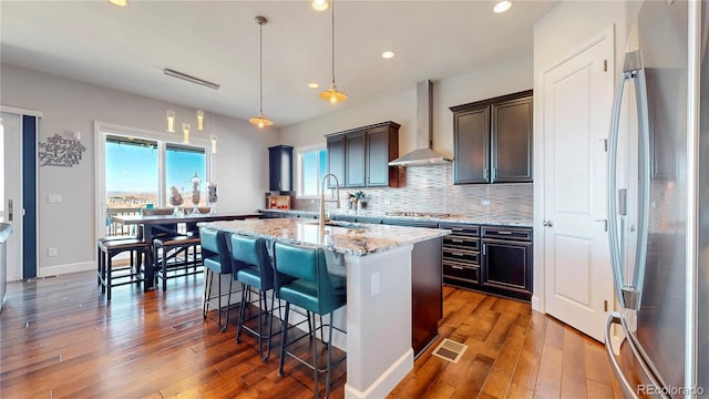 kitchen with a sink, appliances with stainless steel finishes, backsplash, wall chimney exhaust hood, and an island with sink