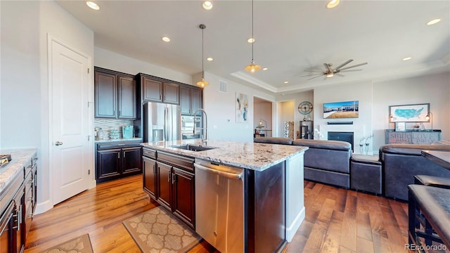 kitchen featuring stainless steel appliances, a glass covered fireplace, a sink, light stone countertops, and light wood-type flooring