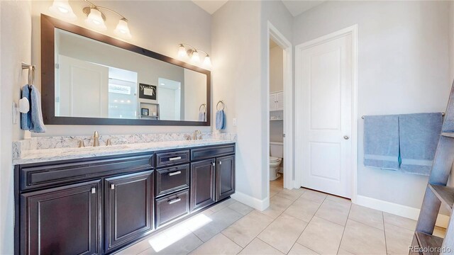 bathroom featuring baseboards, a sink, toilet, and double vanity