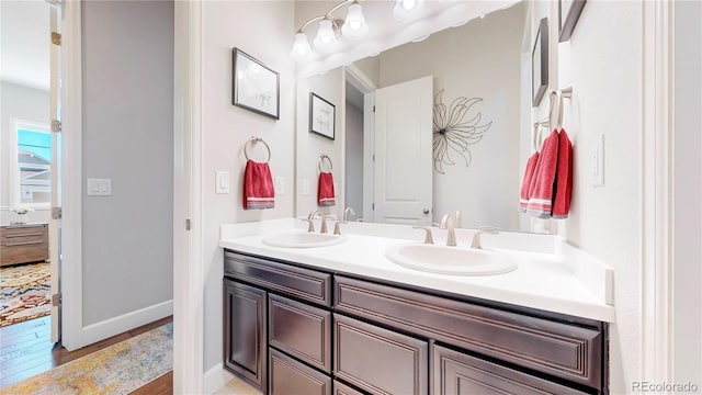 full bath featuring double vanity, wood finished floors, a sink, and baseboards