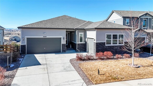 view of front facade with a garage, stone siding, a shingled roof, and concrete driveway