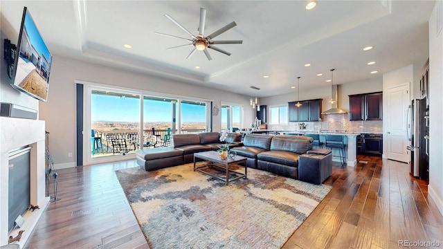 living area featuring baseboards, a raised ceiling, a glass covered fireplace, dark wood-style floors, and recessed lighting