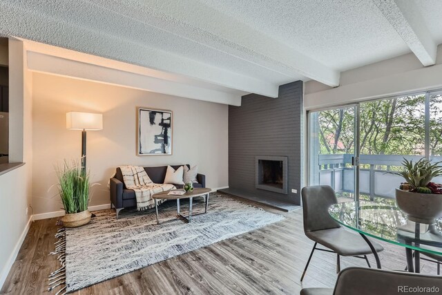 living room featuring a brick fireplace, a textured ceiling, hardwood / wood-style floors, and beamed ceiling