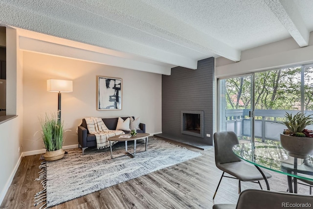 living room with beamed ceiling, wood-type flooring, a fireplace, and a textured ceiling