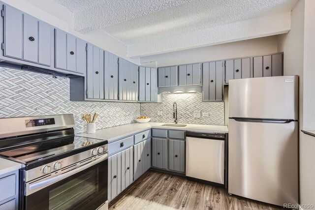 kitchen with decorative backsplash, a textured ceiling, hardwood / wood-style floors, appliances with stainless steel finishes, and sink