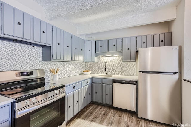 kitchen with sink, light hardwood / wood-style flooring, a textured ceiling, stainless steel appliances, and backsplash