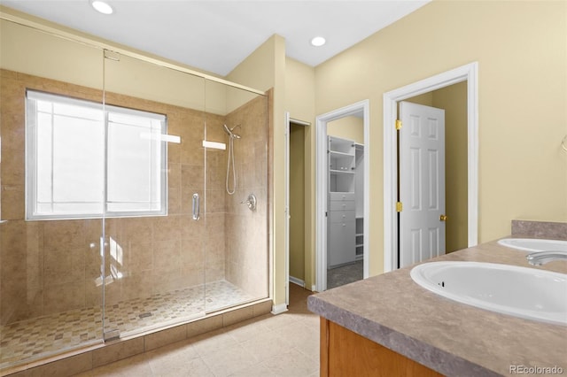 bathroom featuring double vanity, a stall shower, tile patterned floors, a walk in closet, and a sink