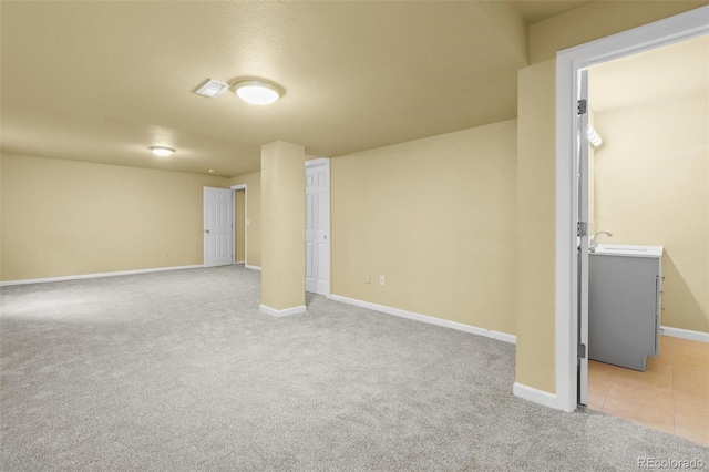 basement featuring baseboards, light tile patterned floors, a sink, and light colored carpet