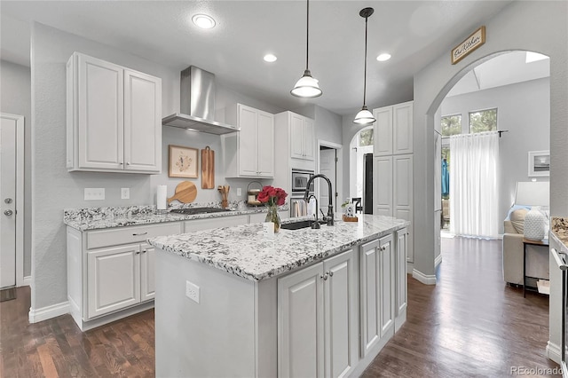 171 Columbine St, Larkspur, CO 80118 - kitchen featuring wall chimney range hood, arched walkways, white cabinets, dark wood-style flooring, and recessed lighting