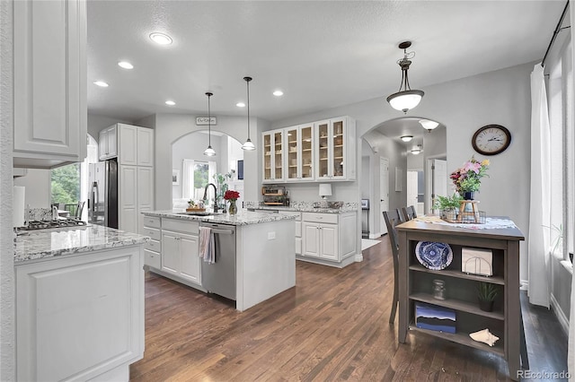 171 Columbine St, Larkspur, CO 80118 - kitchen featuring arched walkways, appliances with stainless steel finishes, a kitchen island with sink, white cabinetry, and dark wood-type flooring