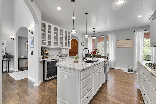 171 Columbine St, Larkspur, CO 80118 - kitchen with wine cooler, arched walkways, glass insert cabinets, white cabinetry, and plenty of natural light