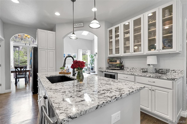 171 Columbine St, Larkspur, CO 80118 - kitchen with arched walkways, dark wood-style floors, light stone counters, a kitchen island with sink, and white cabinetry