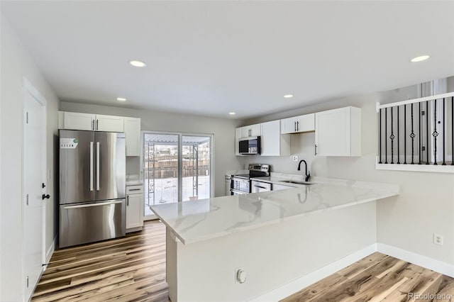 kitchen with white cabinetry, sink, light hardwood / wood-style floors, kitchen peninsula, and stainless steel appliances