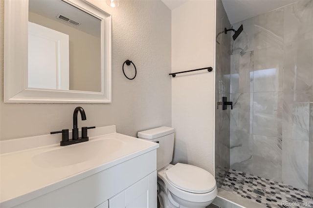 bathroom with vanity, tiled shower, and toilet