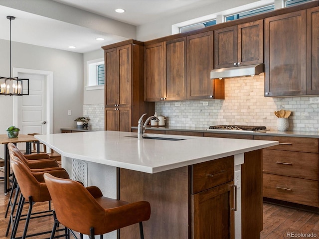 5511 Wabash St, Denver, CO 80238 - kitchen with under cabinet range hood, dark wood-type flooring, decorative backsplash, a kitchen bar, and light countertops