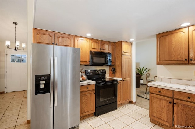 kitchen with decorative light fixtures, an inviting chandelier, tile countertops, light tile patterned floors, and black appliances