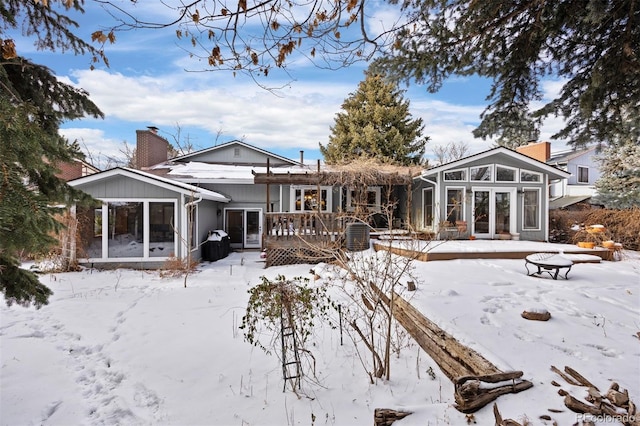 snow covered back of property with a sunroom and a wooden deck