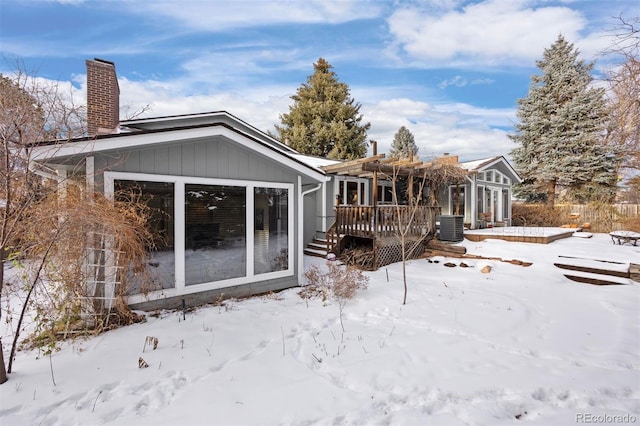 snow covered house with a deck, cooling unit, and a sunroom