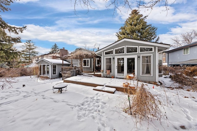 snow covered rear of property with a sunroom and a wooden deck