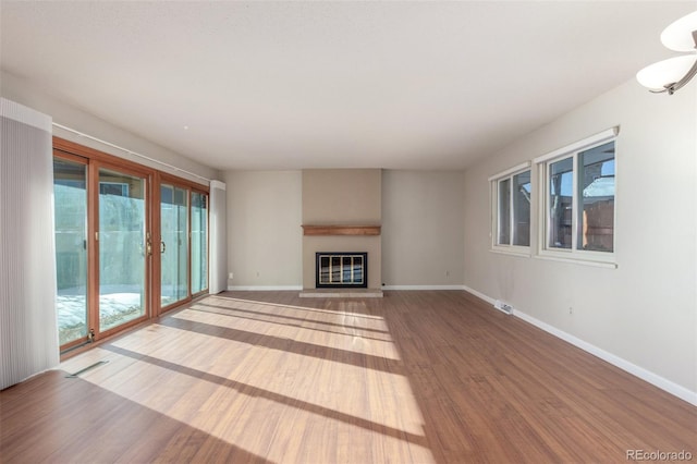 unfurnished living room featuring visible vents, baseboards, wood finished floors, and a glass covered fireplace