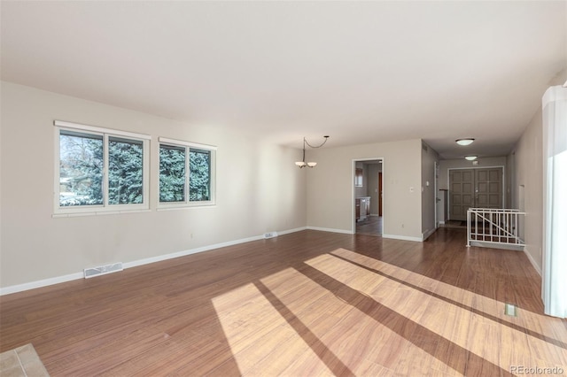 empty room with dark wood-style flooring, an inviting chandelier, visible vents, and baseboards