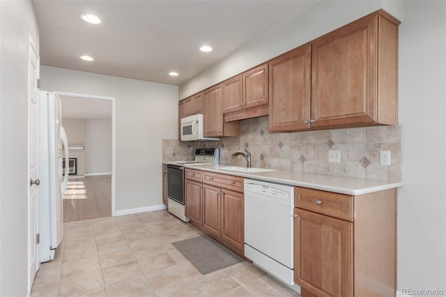 kitchen featuring white appliances, tasteful backsplash, brown cabinetry, light countertops, and a sink