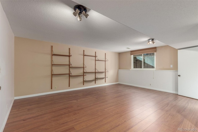 empty room featuring a textured ceiling, wood finished floors, and baseboards