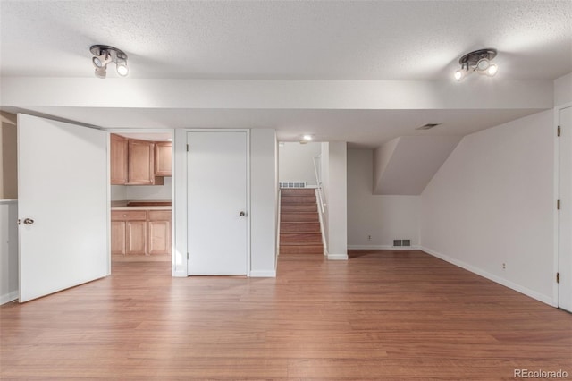 additional living space with a textured ceiling, light wood finished floors, and visible vents