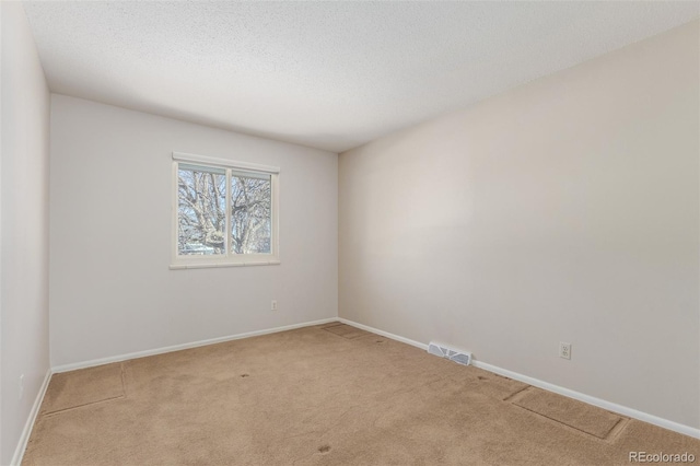 unfurnished room featuring light colored carpet, visible vents, a textured ceiling, and baseboards