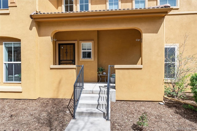 view of exterior entry featuring a tiled roof, stucco siding, and covered porch