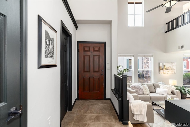 foyer featuring baseboards, ceiling fan, a healthy amount of sunlight, and a towering ceiling
