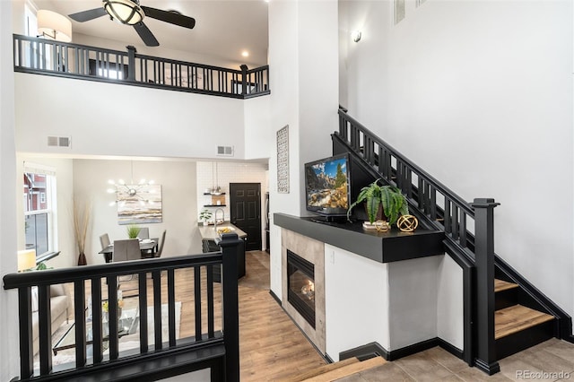stairway featuring visible vents, a glass covered fireplace, ceiling fan with notable chandelier, and a towering ceiling