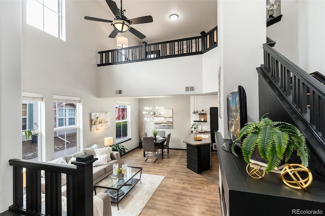 living area featuring a high ceiling, ceiling fan with notable chandelier, stairs, and visible vents