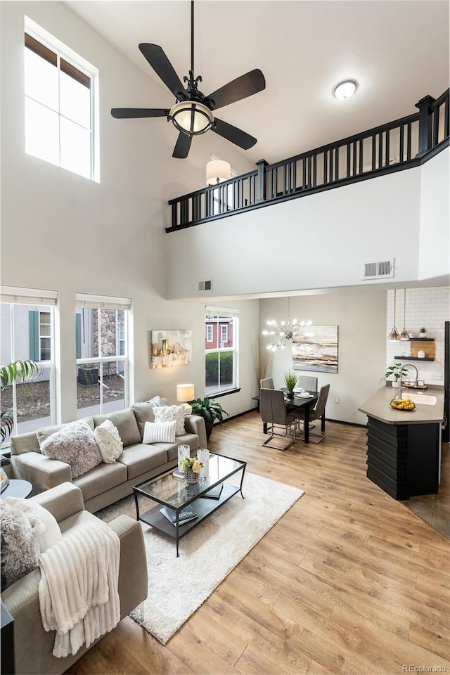 living room featuring ceiling fan with notable chandelier, a high ceiling, and a healthy amount of sunlight