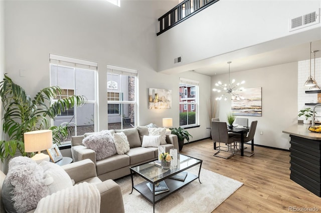 living room featuring visible vents, light wood-style flooring, an inviting chandelier, and a towering ceiling