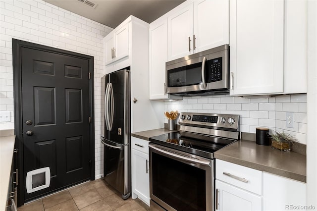 kitchen with dark countertops, appliances with stainless steel finishes, white cabinetry, light tile patterned floors, and backsplash