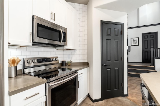 kitchen featuring light tile patterned floors, appliances with stainless steel finishes, white cabinets, and backsplash