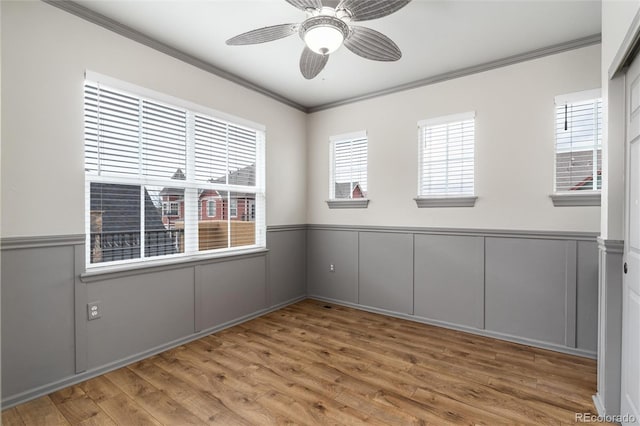 spare room with a ceiling fan, wainscoting, wood finished floors, ornamental molding, and a decorative wall