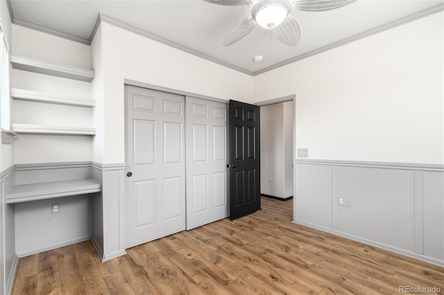 unfurnished bedroom featuring crown molding, a closet, wood finished floors, a wainscoted wall, and a ceiling fan