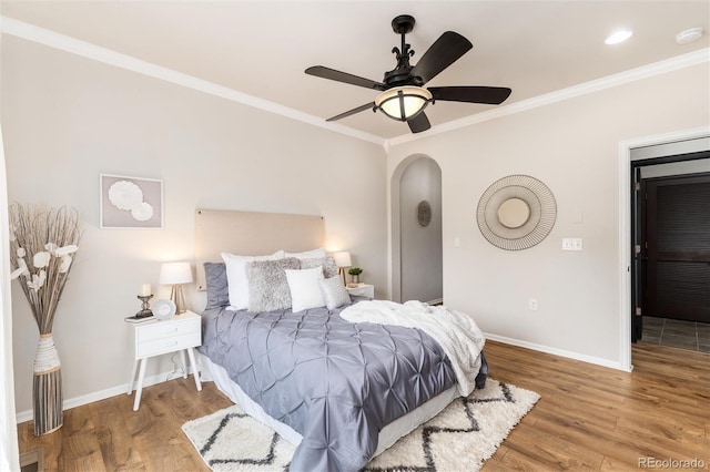 bedroom featuring crown molding, arched walkways, baseboards, and wood finished floors