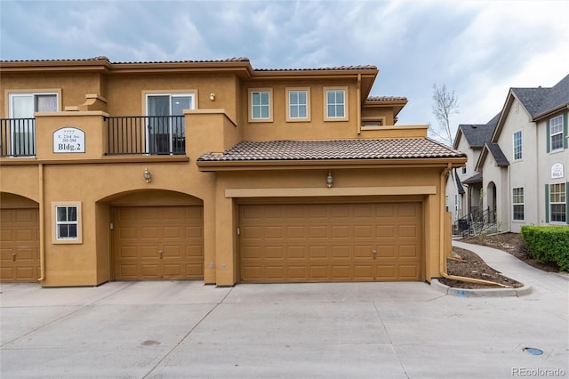 view of front of home featuring an attached garage, a tile roof, stucco siding, a balcony, and driveway