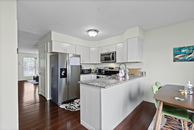 kitchen with stainless steel appliances, a peninsula, dark wood-style floors, and light stone counters