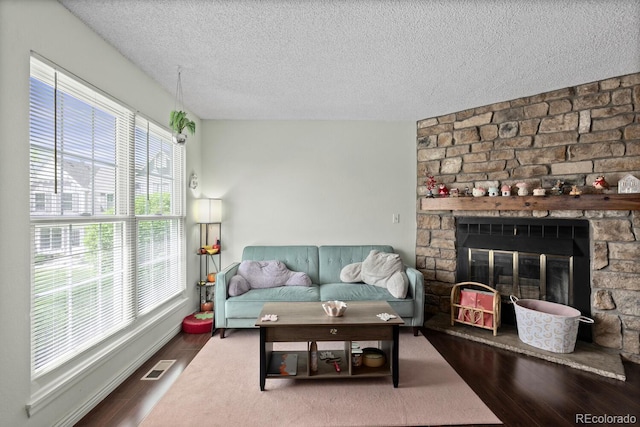 living area featuring a textured ceiling, wood finished floors, and a stone fireplace