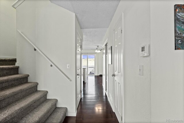 hallway with a textured ceiling, stairway, baseboards, and dark wood-type flooring