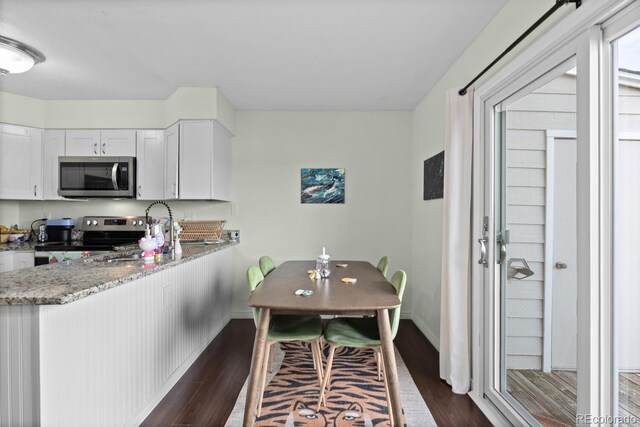 kitchen with appliances with stainless steel finishes, dark wood-style floors, light stone counters, and baseboards