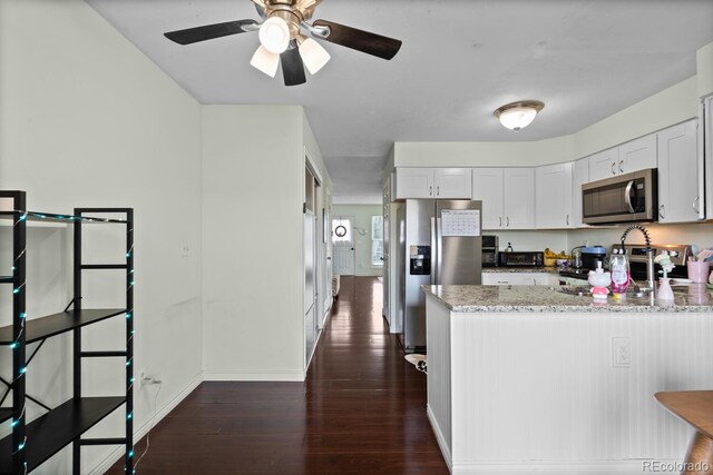 kitchen with stainless steel appliances, dark wood-style flooring, a peninsula, light stone counters, and baseboards