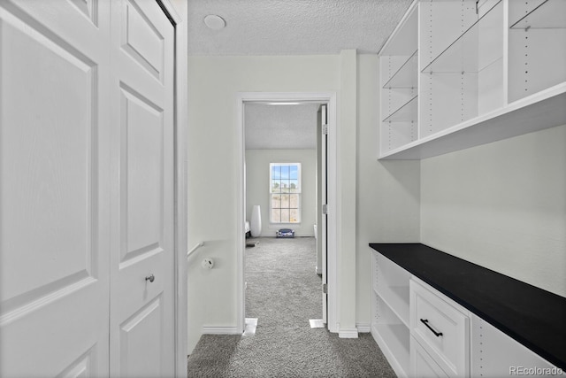 hall with a textured ceiling, carpet floors, and baseboards