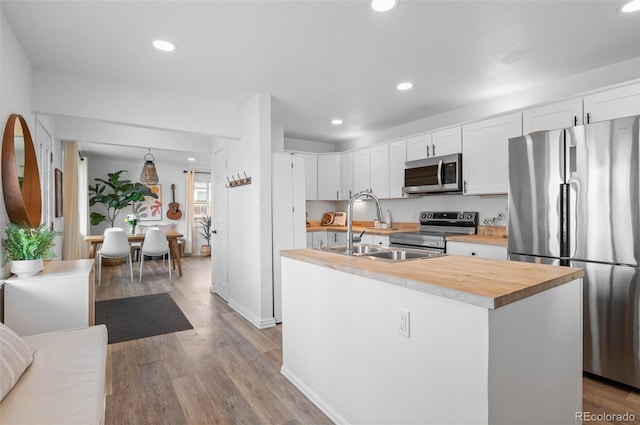 kitchen with appliances with stainless steel finishes, white cabinetry, sink, a center island with sink, and light wood-type flooring