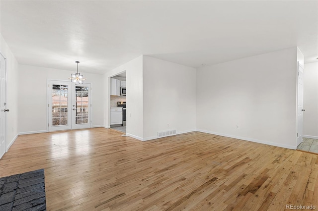 unfurnished living room with a chandelier, french doors, and light hardwood / wood-style flooring